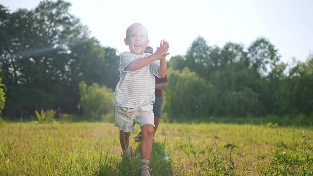 Father throws soccer ball to son. Son catches soccer ball. Boy playing football runs. Father and child enjoy football. Soccer ball bounces high. Father smiles at son. Happy boy loves football.