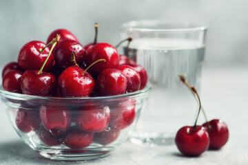 Fresh Cherries in Glass Bowl with Water Glass on Light Surface