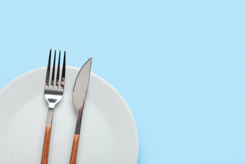 Plate with silver fork and knife on blue background