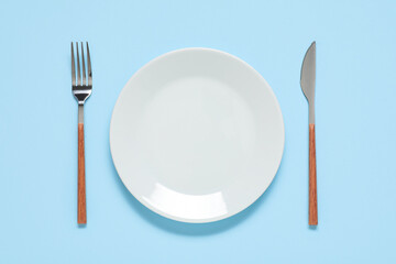 Plate with silver fork and knife on blue background