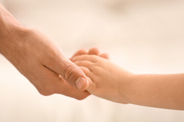 Little girl with her father holding hands at home, closeup