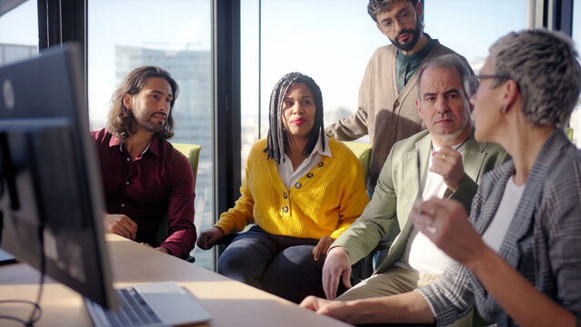 Diverse group gathers around a screen for a collaborative discussion as a middle aged businesswoman leads the conversation sharing ideas guiding colleagues during a strategy meeting in a modern office