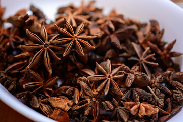 Close-up of star anise seeds in a white bowl, aromatic dried spices for cooking and traditional medicine, organic herbal seasoning concept, macro photography.