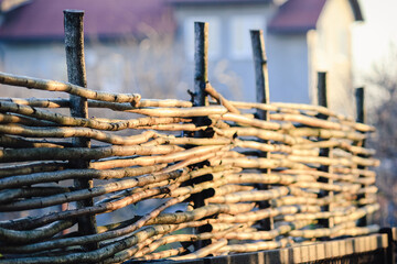 A rustic wicker fence made of wooden branches glowing in the warm golden sunlight of a peaceful garden © emerald17