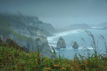Muroran, Hokkaido, Japan - Oct 04 2024, panoramic aerial view of the picturesque Pacific ocean coast with sharp cliffs and high mountain slopes, in a storm, it's raining, at daytime, Muroran, Japan