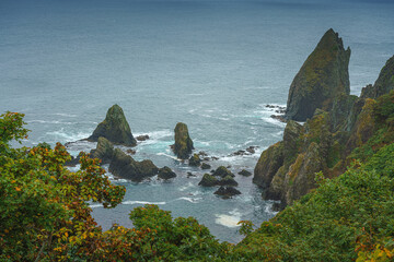 Muroran, Hokkaido, Japan - Oct 04 2024, panoramic aerial view of the picturesque Pacific ocean coast with sharp cliffs and high mountain slopes, in a storm, it's raining, at daytime, Muroran, Japan
