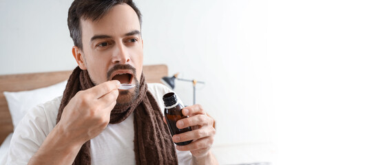 Ill young man taking cough syrup in bedroom, closeup