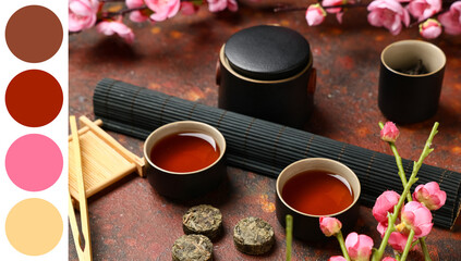 Teapot with cups of tea, dry pressed puer leaves, bamboo mat, tongs and plum blossom branches on red grunge background