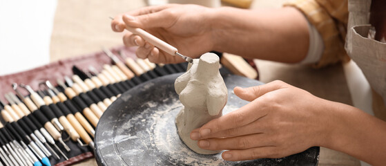 Female sculptor making clay figurine on pottery wheel in workshop, closeup