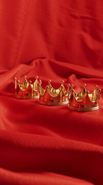 Three golden crowns on red silk fabric background. Royal luxury and power concept video.