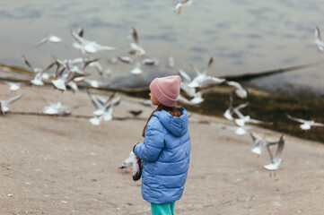A beautiful teenage girl, a dreamy child, walks along the embankment against the backdrop of the sea, feeding birds and seagulls.