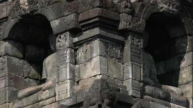 Two statues of sitting Buddha in niches carved from dark volcanic rock. Decorative details of 9th century Borobudur Mahayana Buddhist temple in Magelang, Central Java, Indonesia. Panning video.