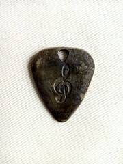 Metal brass guitar pick with treble clef engraving on transparent background