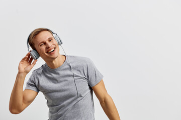 Smiling young man listening to music with headphones, casual grey t-shirt, enjoying music, cheerful...