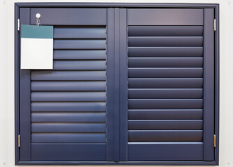 Fototapeta premium Dark blue folding plantation shutters covering a window with a blank sample tag, showing home decor and privacy