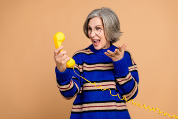 Aged mature woman with yellow telephone smiles in a blue striped sweater for advertising and...