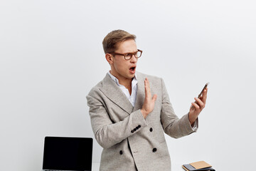 Modern young man in glasses wearing a grey business suit with a surprised expression looking at his...