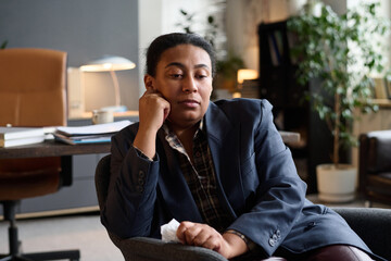 Portrait of Black woman sitting in therapy office resting head on hand holding tissue looking contemplative showing emotion during counseling session