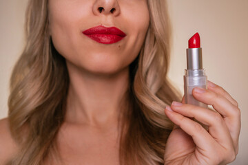 Close-up of young blonde woman holding red lipstick near her lips. Elegant beauty portrait with...