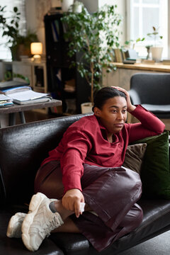 Black woman reclining on sofa during therapy session, resting head on hand and looking thoughtful, indoor office setting with plants and documents visible in background