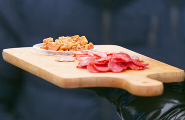 Tasting samples of sliced sausage and traditional pork cracklings served on a wooden board at the Naplavka farmers market in Prague, inviting visitors to try local cured meats.