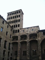 Fototapeta premium Exterior view of a tall, historic medieval stone tower with multiple rows of arched windows adjacent to an ancient palace complex in the Gothic Quarter of a city