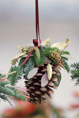 Handmade Christmas ornament made of pine cone, evergreen branches and dried plants hanging at...