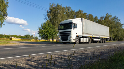 White semi-truck with a fully loaded cargo trailer driving along countryside road. The lorry travels on an empty freeway.