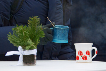 Cold winter morning at Prague Naplavka farmers market. A bundled visitor enjoys a steaming hot drink at a simple table, advent greenery adding warmth, comfort and seasonal charm to the scene.