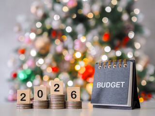 Wooden blocks with the number 2026 on stack of coins and Desk calendar with shiny light for Christmas background. The concept about budget planning and allocation in year 2026