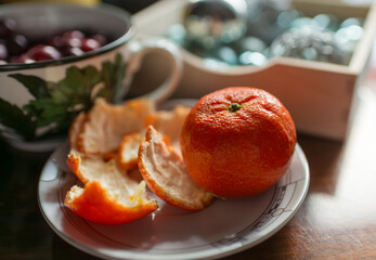 Ripe mandarin orange with aromatic peel and separated segments on a patterned plate. Warm natural light and soft bokeh create a cozy seasonal mood for healthy snack, citrus freshness, and food styling