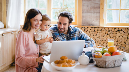 Young family of three with little small kid child toddler infant talking on videocall conversation meeting online on laptop while having breakfast. Parenthood and adoption