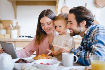 Child developing cartoons video. Caucasian happy parents watching animated movies, having videocall with grandparents on tablet with kid child toddler infant at home kitchen