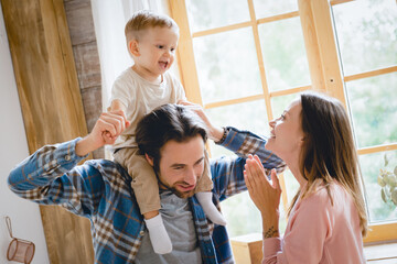 Happy caucasian young parents mother and father playing having fun with their small little kid child toddler infant baby at home kitchen. Baby care and parenthood. Adoption concept