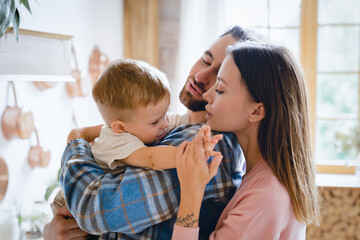 Adoption and IVF concept. Parenthood. Caucasian young happy parents taking care of little small child kid toddler infant at home kitchen, hugging and embracing together