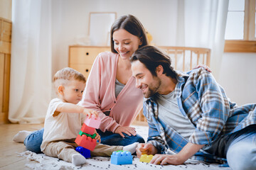 Young happy family parents playing with blocks at home with little small toddler kid child son daughter infant new born baby, developing imagination skills. Parenthood