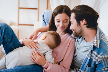 Little small kid child son daughter toddler sleeping on mother`s hands while loving father relaxing spending time with family. Happy moments time together at home. Parenthood