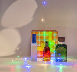 Photo of elegant perfume bottles near a gift box with a yellow ribbon and a string of decorative lights, perfect for a Christmas gift