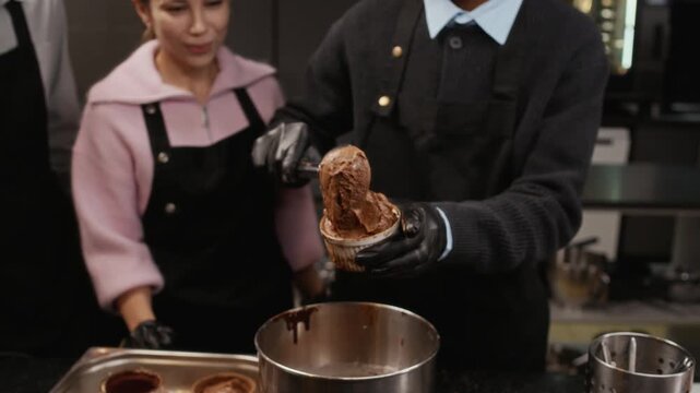 Young African American man filling ceramic mold with portion of chocolate dough using small scoop in culinary class then course trainees congratulating groupmate with applause in restaurant kitchen
