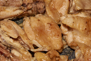 Pieces of chicken meat are fried in a frying pan, exuding flavor and mouth-watering appearance....