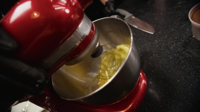 Close up on stand mixer blending batter ingredients while male chef explaining baking techniques to diverse group of culinary course trainees in hands on kitchen class