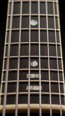 A captivating vertical close-up displaying the rich texture of a guitar's dark wooden fretboard, emphasizing its shimmering metal frets and the distinctive, artistic inlay markers