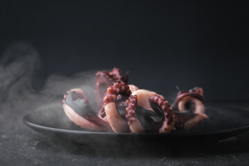 Hot prepared squid or boiled octopus with tentacles wiggling on a plate with steam coming out against black background. Seafood background for a restaurant menu © alexanderon