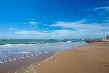 Wide sandy beach with calm sea and blue sky, coastal city on the horizon creating a peaceful seaside landscape with copy space.
