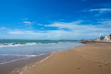 Wide sandy beach with calm sea and blue sky, coastal city on the horizon creating a peaceful seaside landscape with copy space.