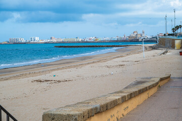 Wide sandy beach with calm sea and blue sky, coastal city on the horizon creating a peaceful seaside landscape with copy space.
