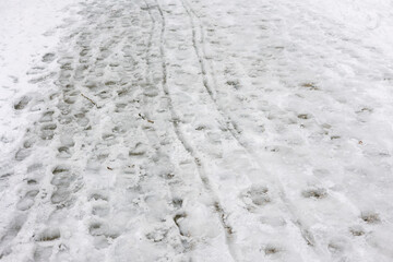 Fototapeta premium Snowy pathway shows tracks from feet and vehicles on a winter day in a city