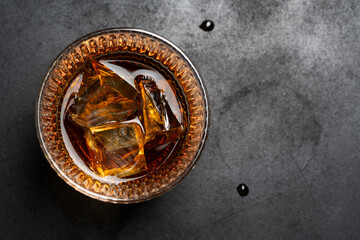 whiskey on the rocks in a glass placed on a dark textured surface