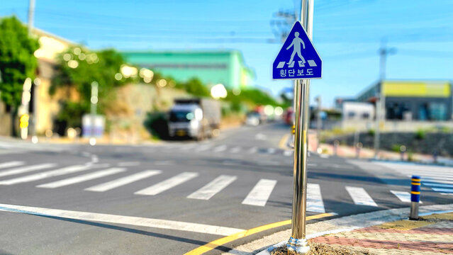 Photo of a traffic sign for a pedestrian crossing at a suburban highway intersection in South Korea with a blurred background