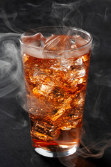 Whiskey Highball with Ice and Smoke on Dark Background. Amber Drink with Ice and Bubbles in a Glass